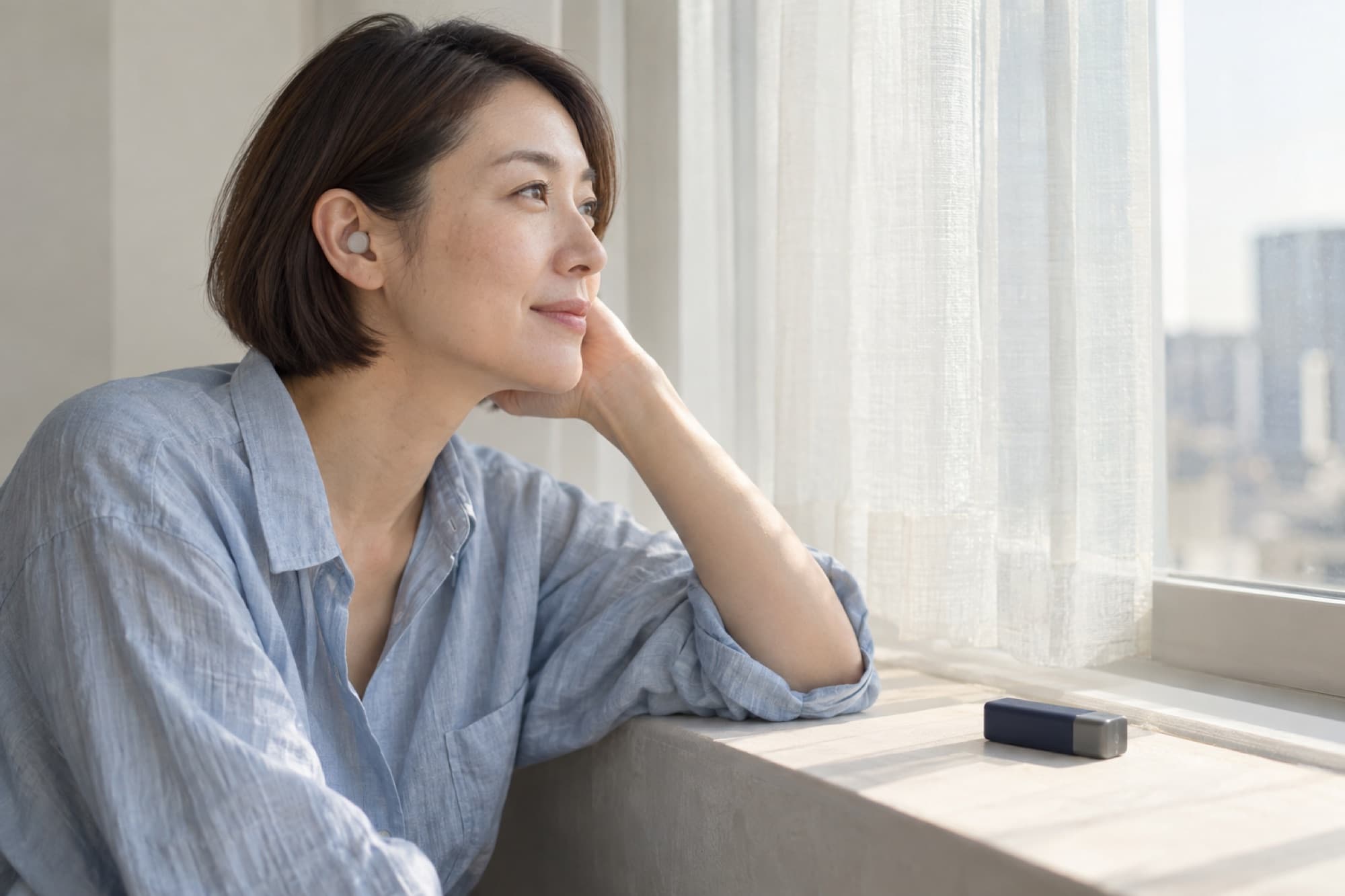 窓辺で外を眺める女性。窓台に Night のアルミケースが置かれている